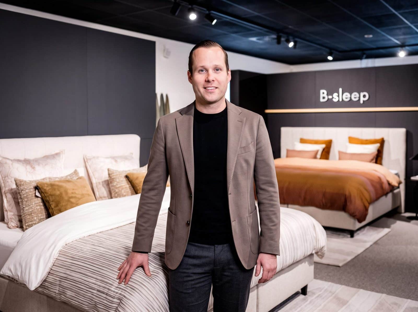 Adviseur van Grisar Slaapcomfort staat in jasje voor een bed in de B-Sleep hoek van de toonzaal