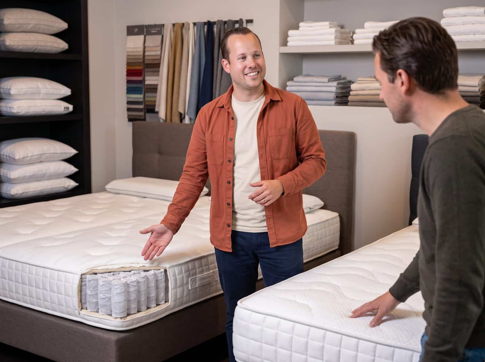 Adviseur in oranje hemd legt de pocketveren van een matras uit aan een klant