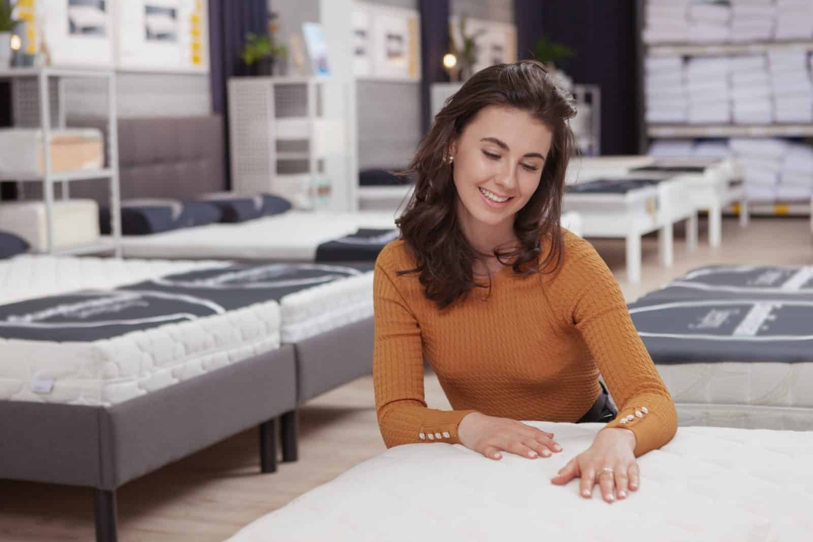Lachende vrouw voelt aan een matras tussen de matrassen in de toonzaal