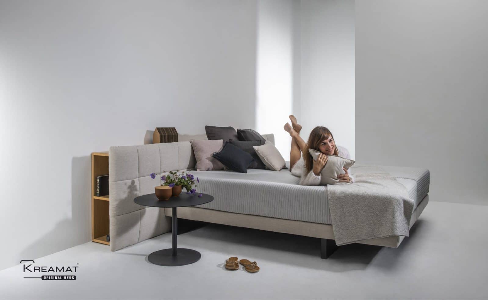 Vrouw ligt te lezen op een bed met sofa-opstelling van Kreamat in een witte ruimte