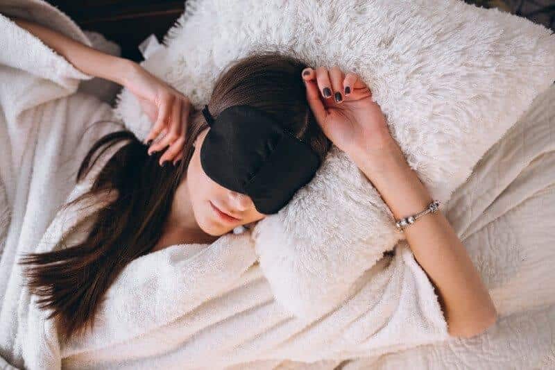 Vrouw met slaapmasker in een bed met een pluizige deken
