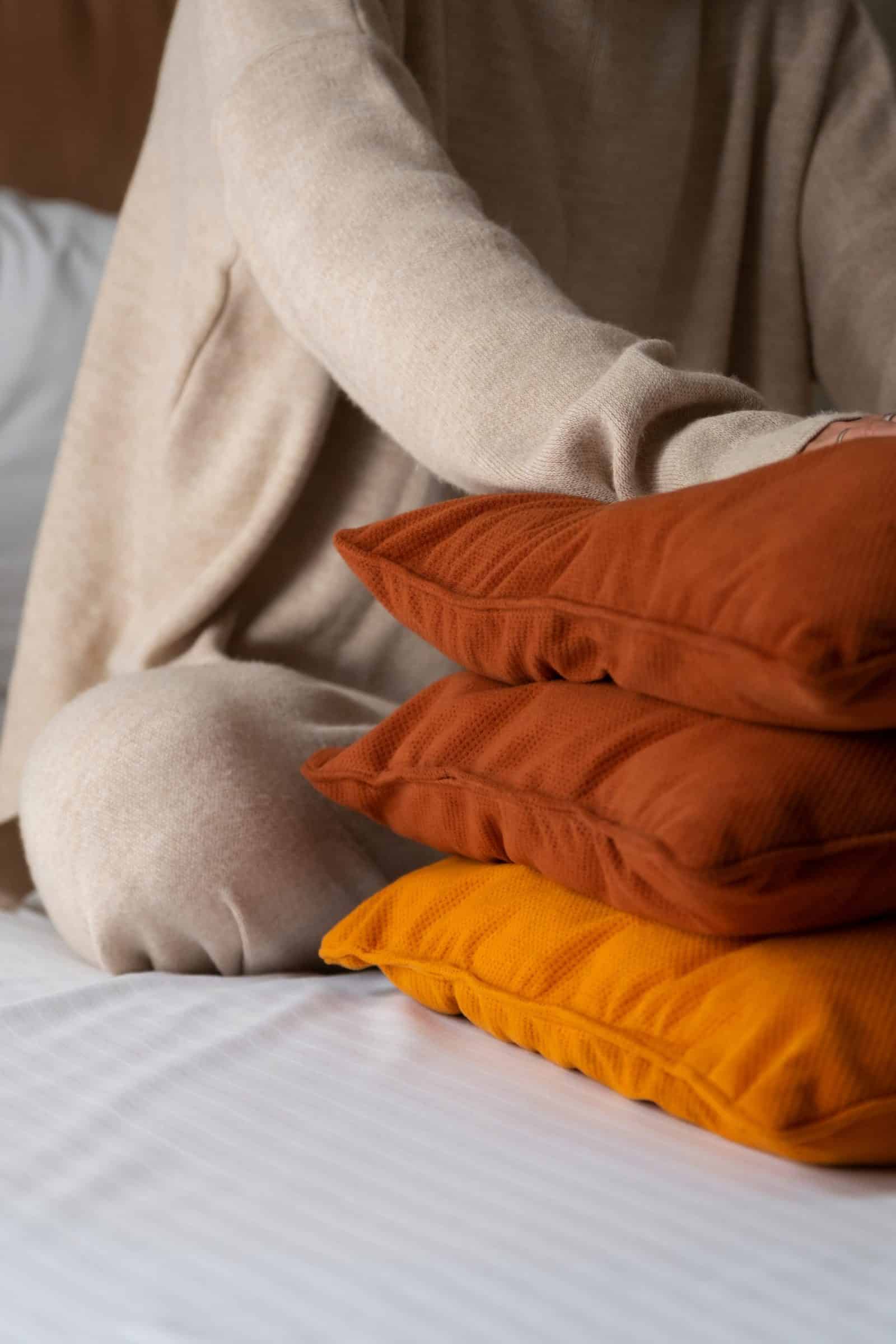 Stapel terracotta en oranje kussens naast iemand in een beige trui