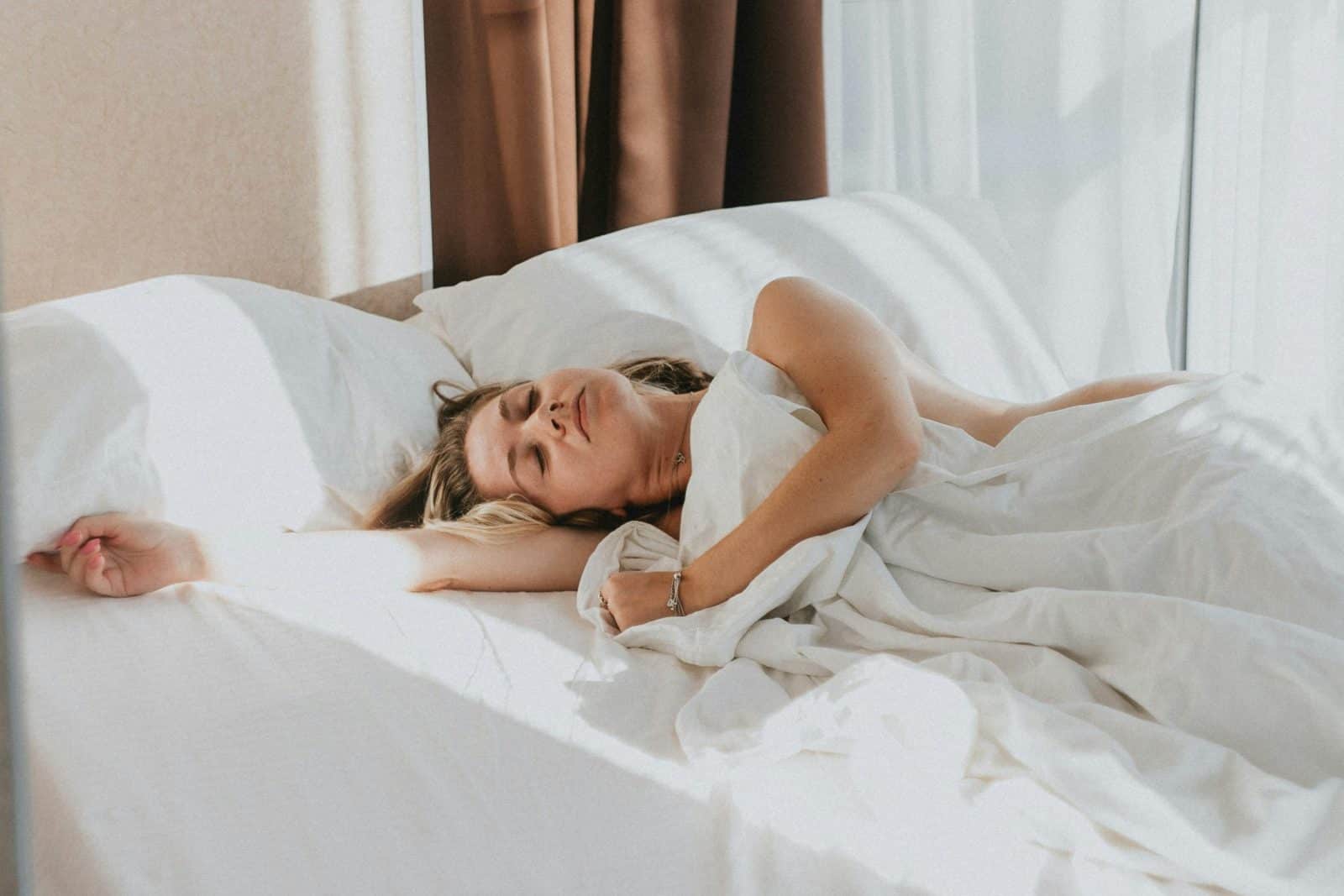Slapende vrouw op een wit hoeslaken met een glad kussen en dekbed