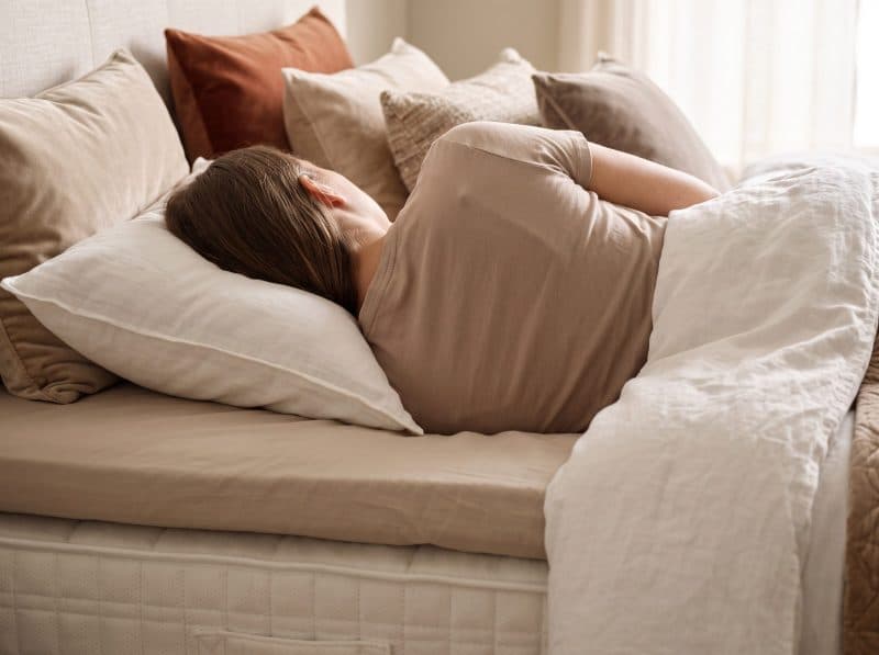 Vrouw slaapt op haar zij op een matras met linnen deken en kussens